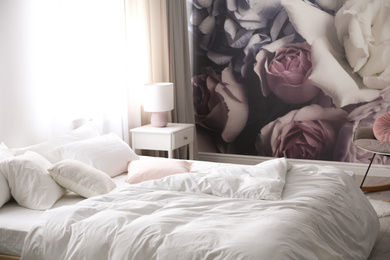Photo of Comfortable bed near wall with floral wallpaper. Stylish room interior