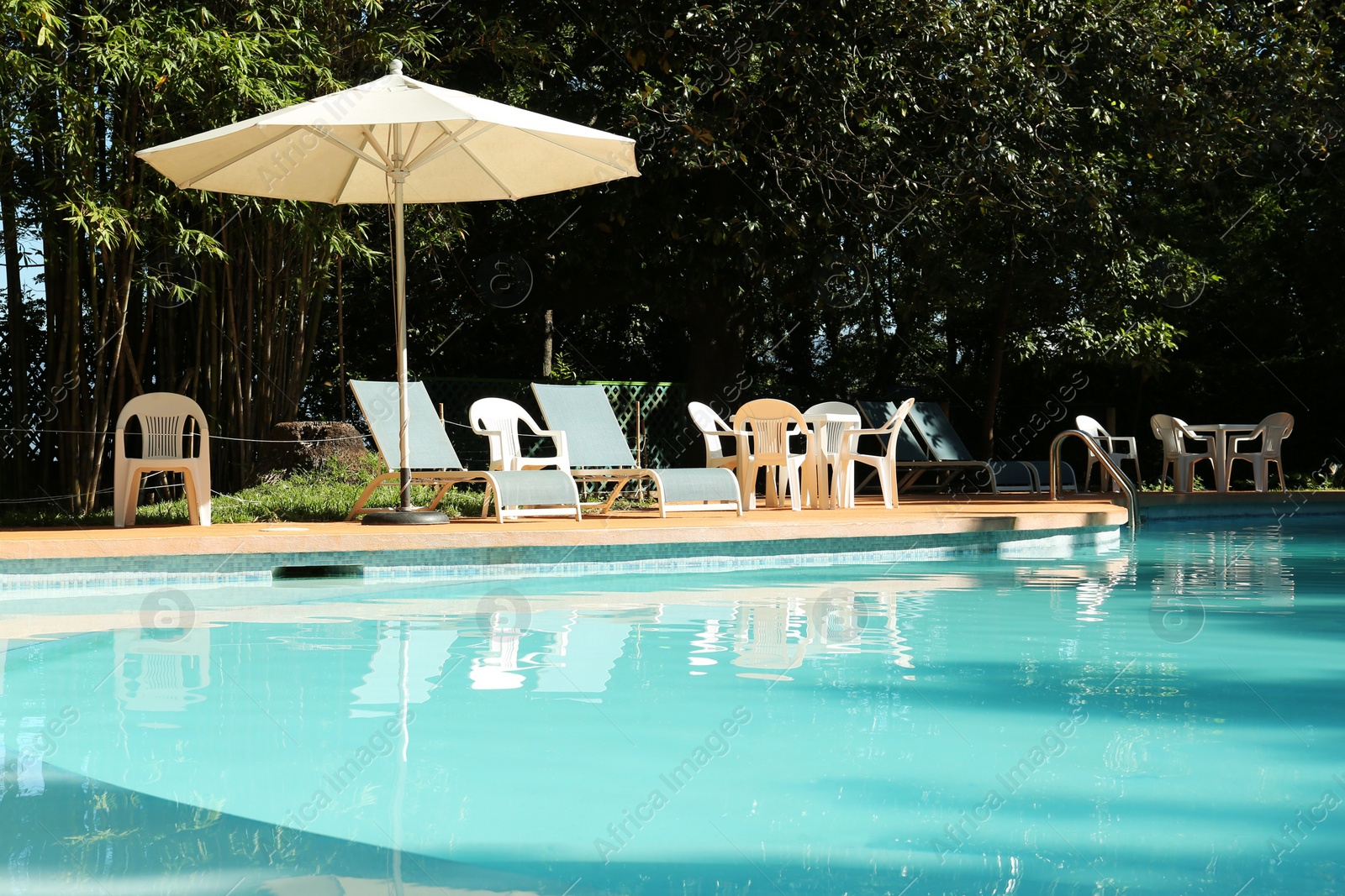 Photo of Pool with clean water, sunbeds and parasol outdoors