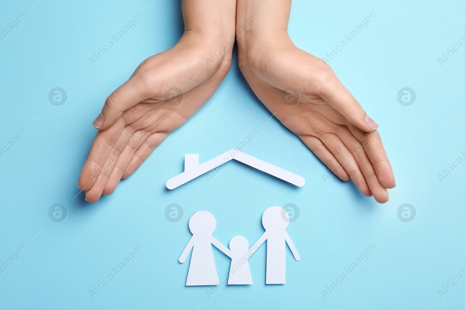 Photo of Woman holding hands over paper silhouettes of family and house roof on color background, top view. Life insurance concept