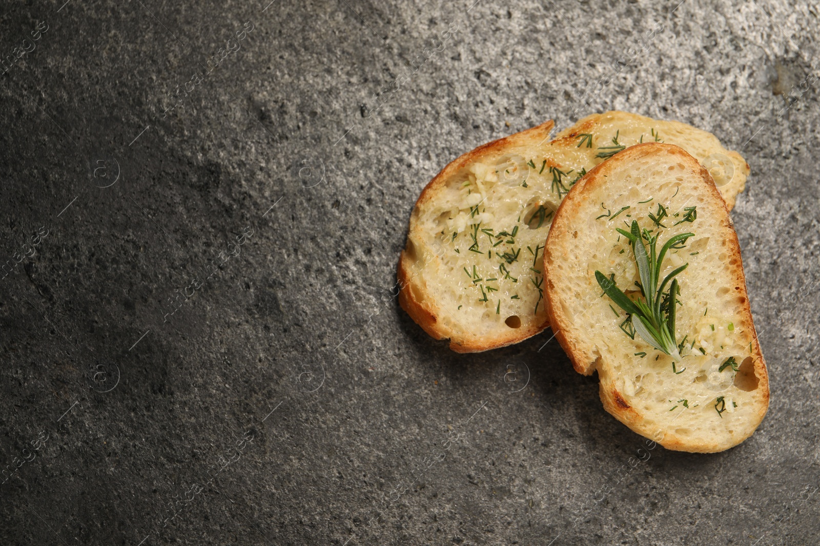 Photo of Tasty baguette with garlic, rosemary and dill on grey textured table, flat lay. Space for text