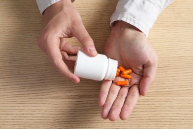 Man pouring pills from bottle at wooden table, top view