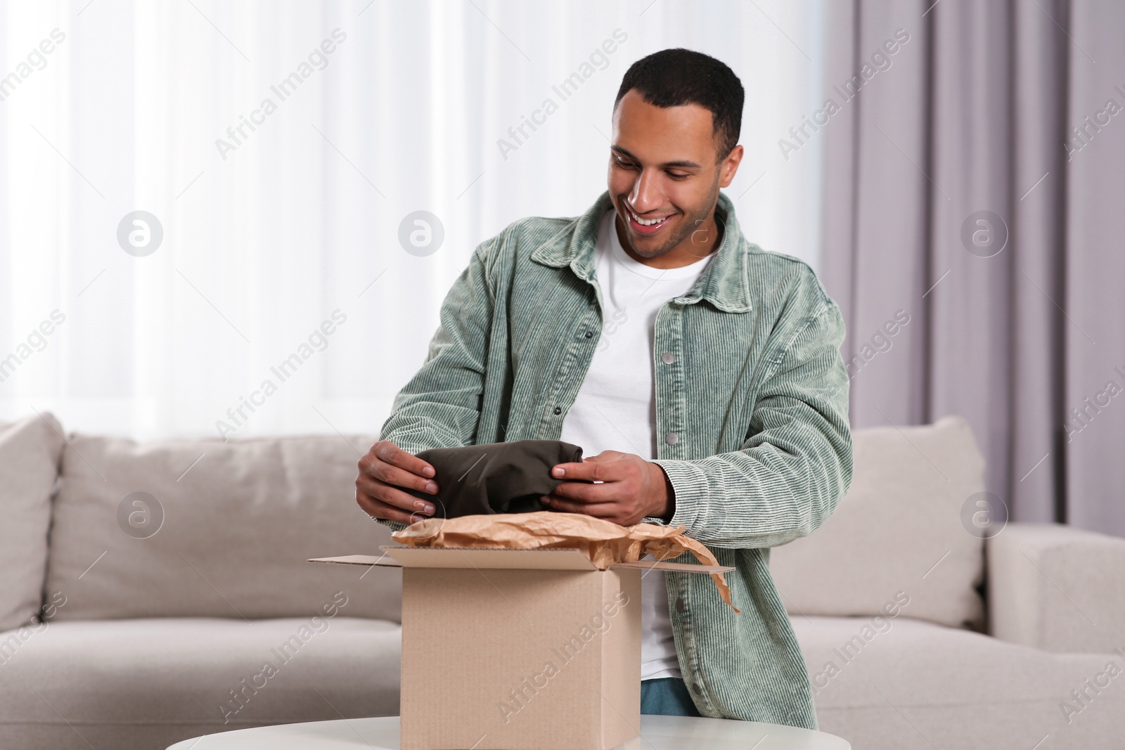 Photo of Happy young man opening parcel at home. Internet shopping