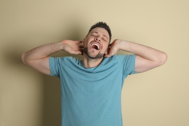 Portrait of sleepy man yawning on beige background