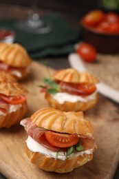 Photo of Delicious profiteroles with cream cheese, jamon and tomato on wooden board, closeup
