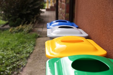 Many colorful recycling bins near brown wall outdoors, closeup. Space for text