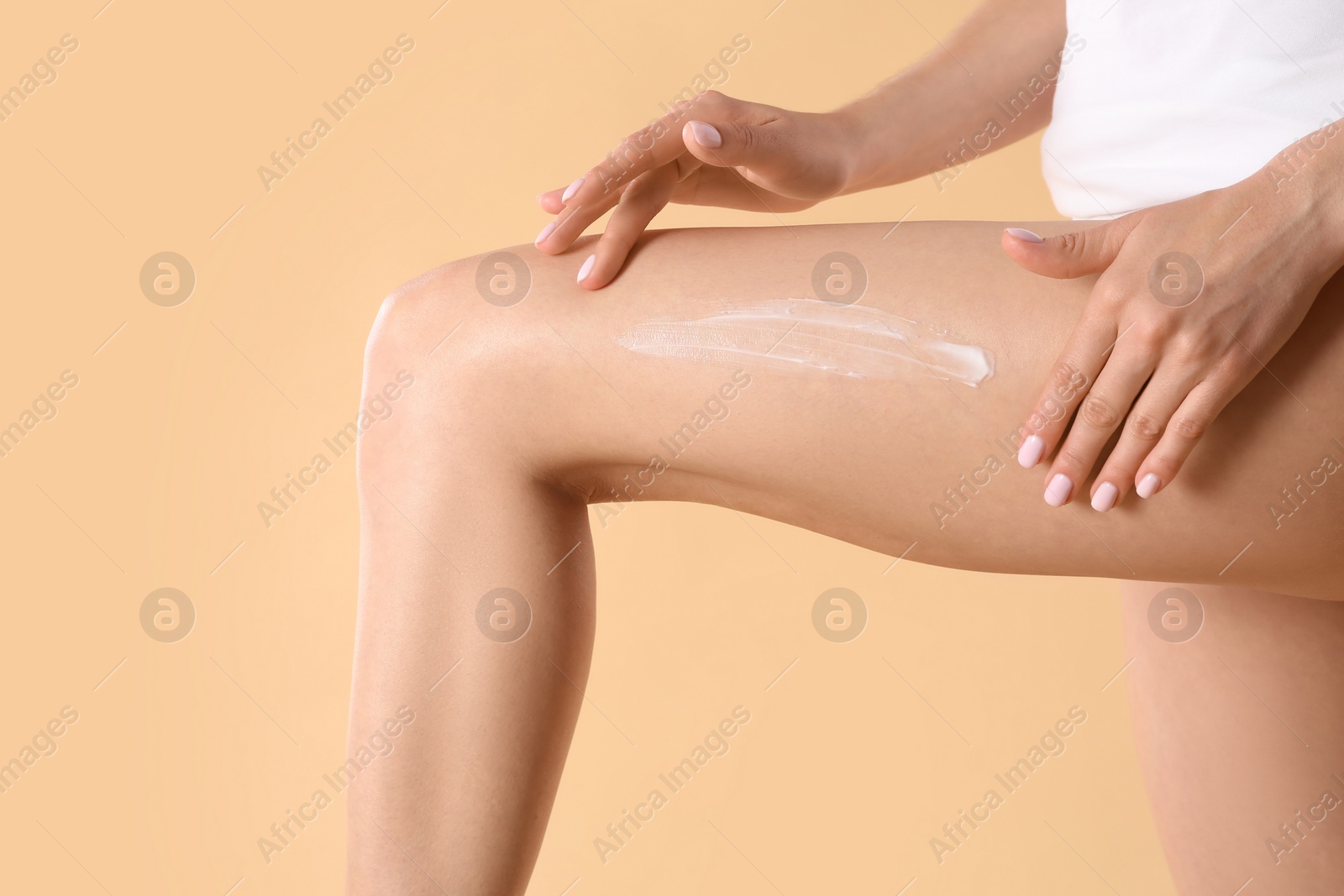 Photo of Woman applying body cream onto her smooth legs on beige background, closeup