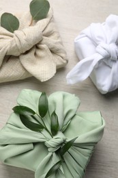 Photo of Furoshiki technique. Gifts packed in different fabrics and decorated with plants on wooden table, flat lay