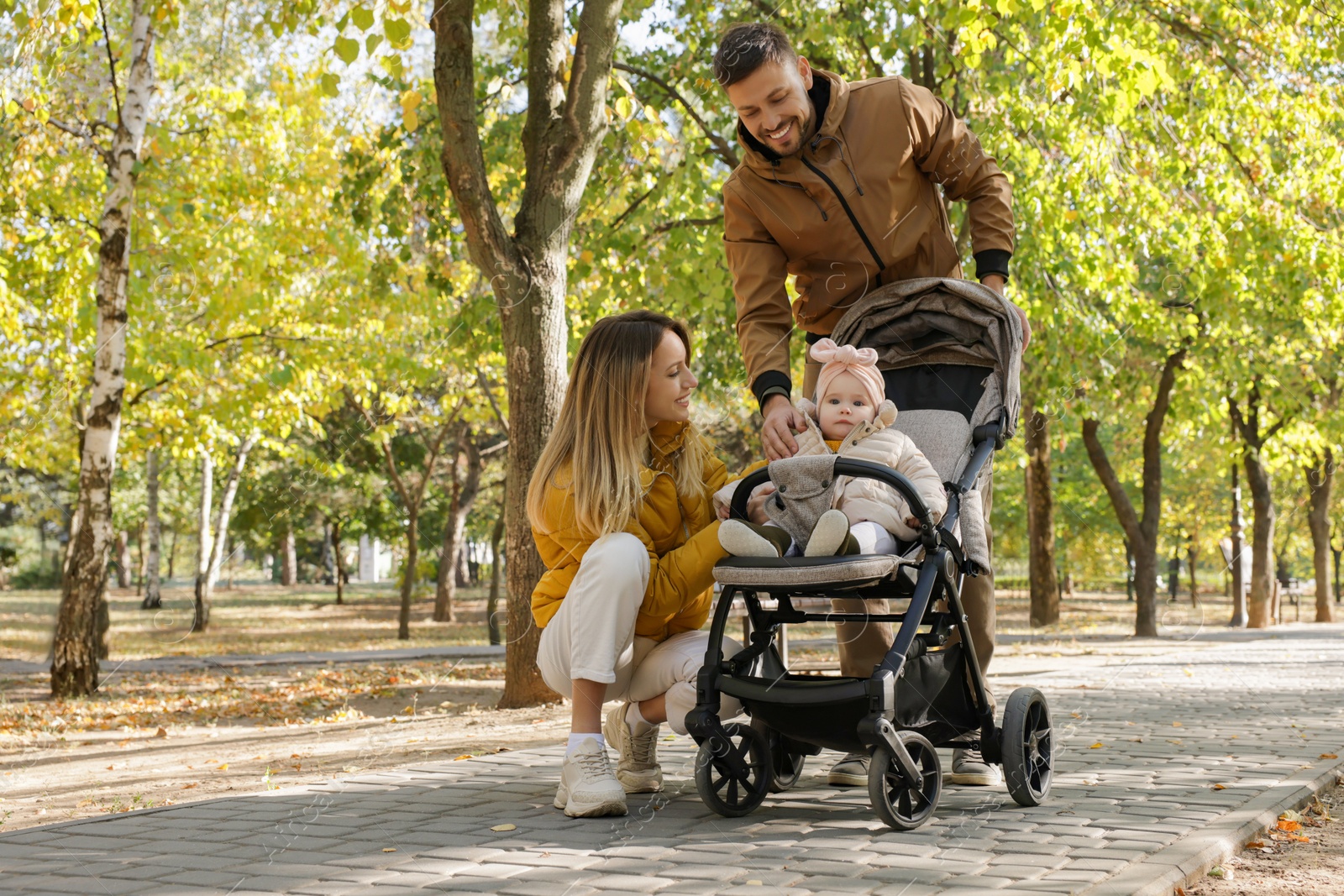 Photo of Happy parents walking with their baby in stroller at park on sunny day