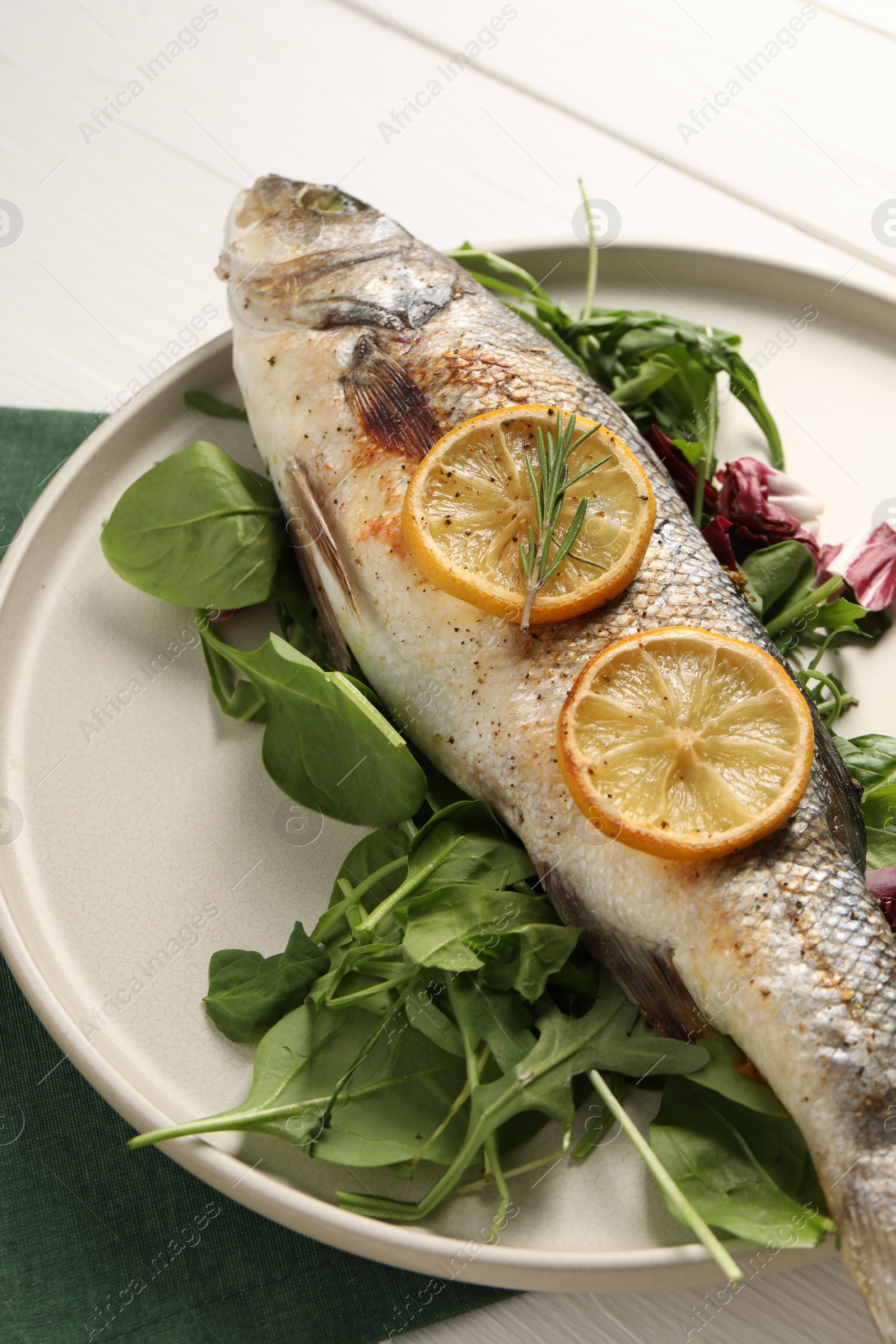 Photo of Baked fish with spinach and lemon on white wooden table, closeup