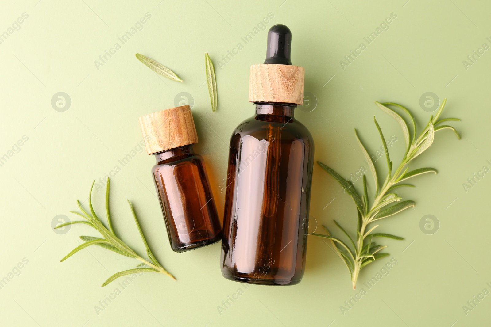 Photo of Aromatic essential oils in bottles and rosemary on green background, flat lay