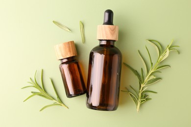 Aromatic essential oils in bottles and rosemary on green background, flat lay