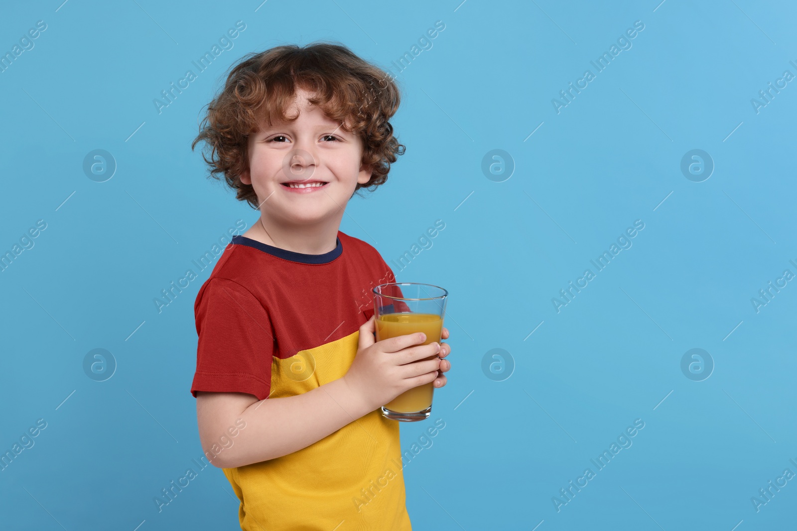 Photo of Cute little boy with glass of fresh juice on light blue background, space for text