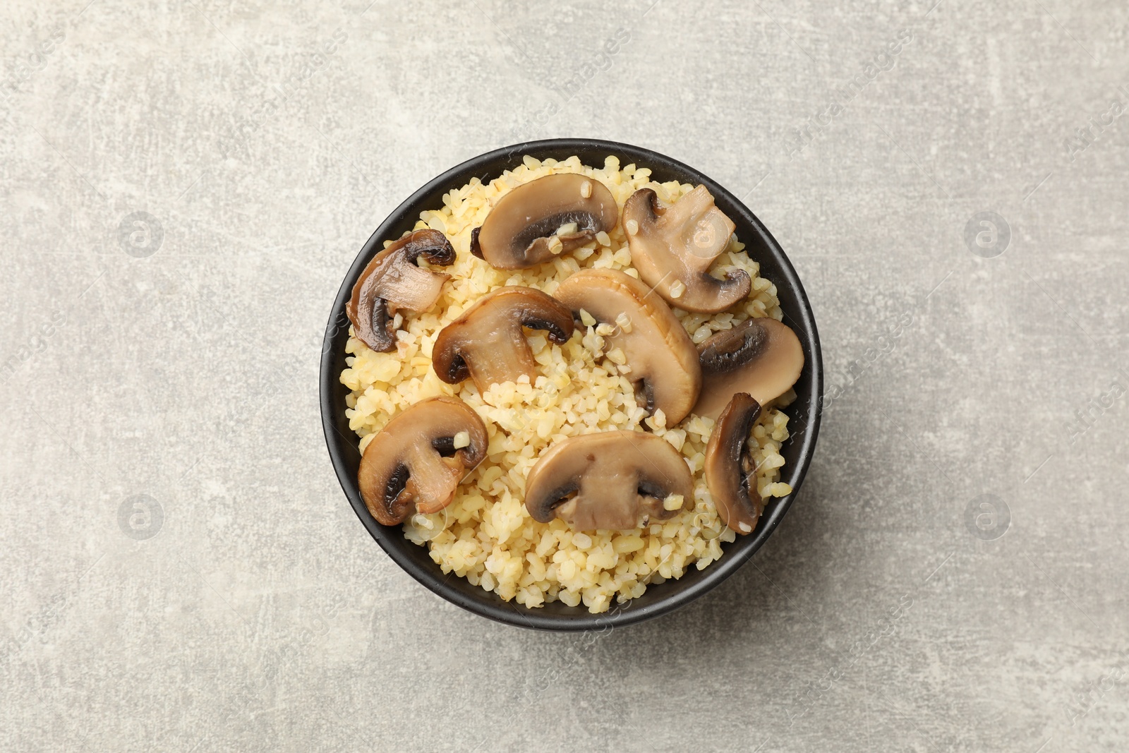 Photo of Delicious bulgur with mushrooms in bowl on gray table, top view