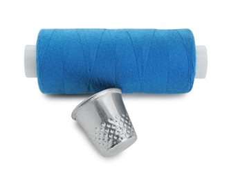 Photo of Thimble and spool of blue sewing thread isolated on white, above view