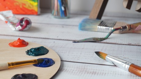 Artist's palette with samples of colorful paints and brushes on white wooden table, closeup
