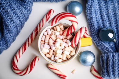 Photo of Cup of tasty cocoa with marshmallows, candy canes and Christmas balls on white table, flat lay