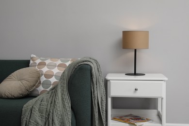 Photo of Stylish lamp on bedside table near sofa in room