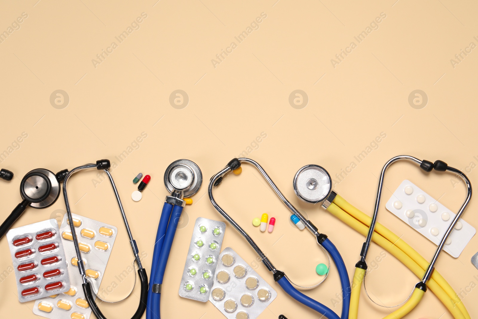 Photo of Stethoscopes and pills on beige background, flat lay. Space for text