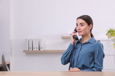 Female receptionist talking on phone at workplace. Space for text