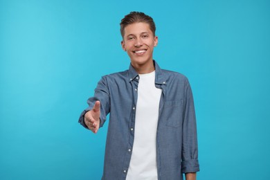 Photo of Happy man welcoming and offering handshake on light blue background