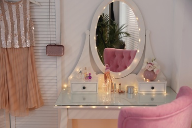 Elegant dressing table with lights and pink chair in stylish room interior