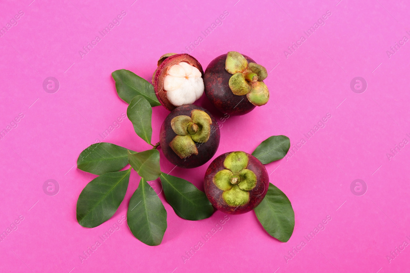 Photo of Fresh ripe mangosteen fruits with green leaves on pink background, flat lay