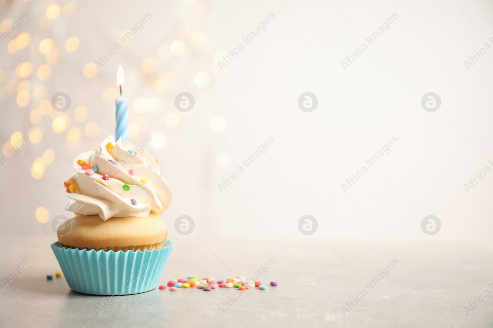Photo of Birthday cupcake with candle on light grey table against blurred lights. Space for text