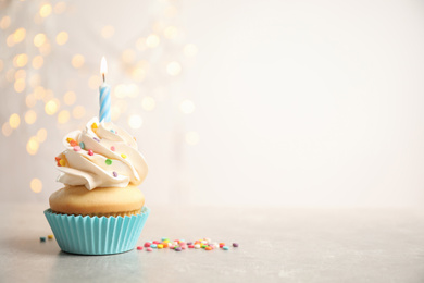 Photo of Birthday cupcake with candle on light grey table against blurred lights. Space for text