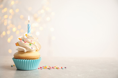 Birthday cupcake with candle on light grey table against blurred lights. Space for text