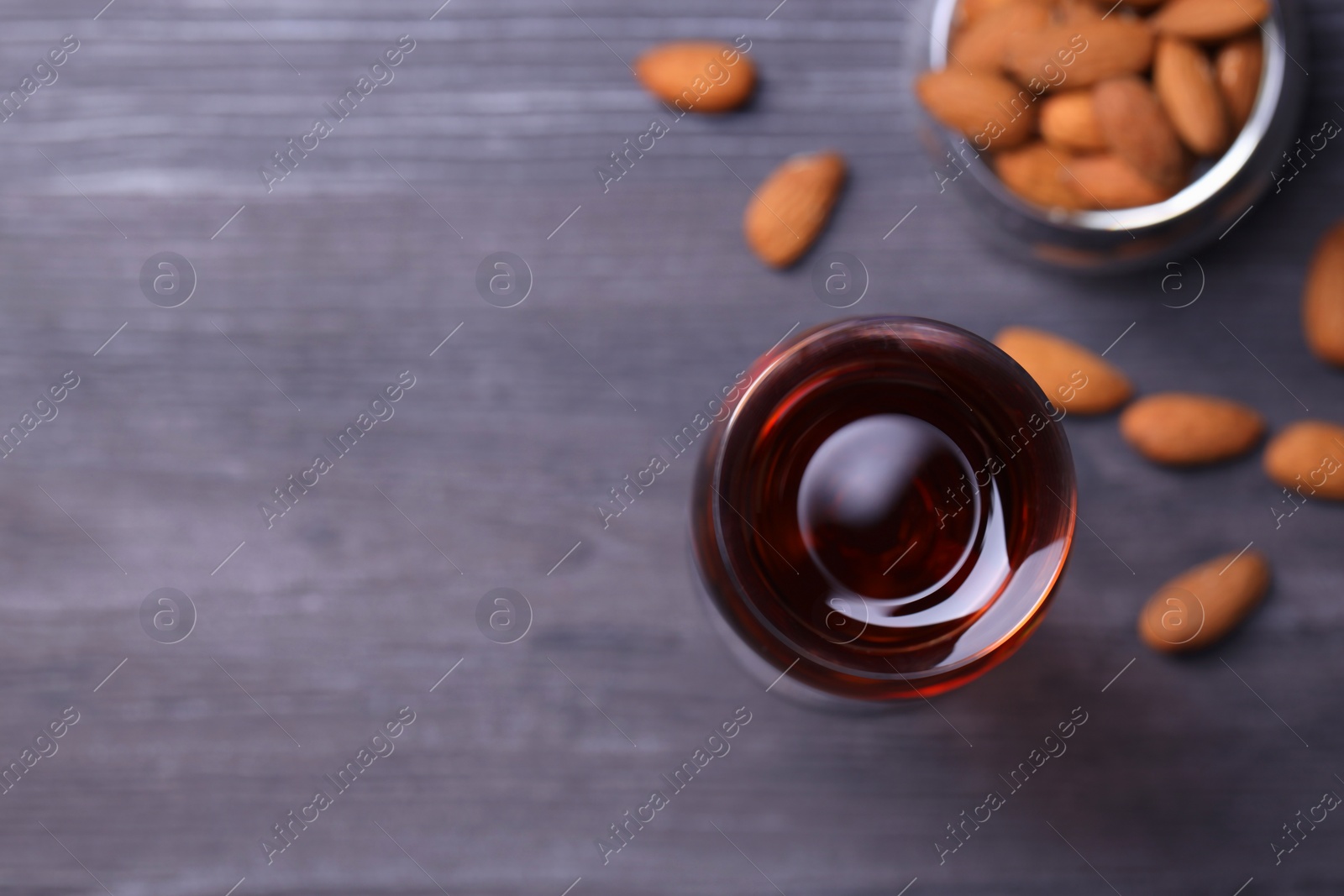 Photo of Liqueur glass with tasty amaretto and almonds on wooden table, flat lay. Space for text