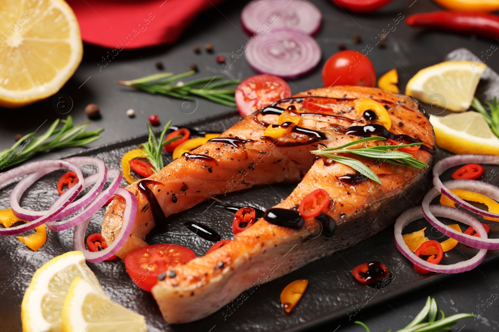 Photo of Slate plate with tasty salmon steak and vegetables on black table, closeup