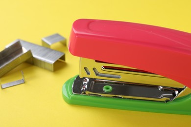 Photo of Bright stapler with staples on yellow background, closeup