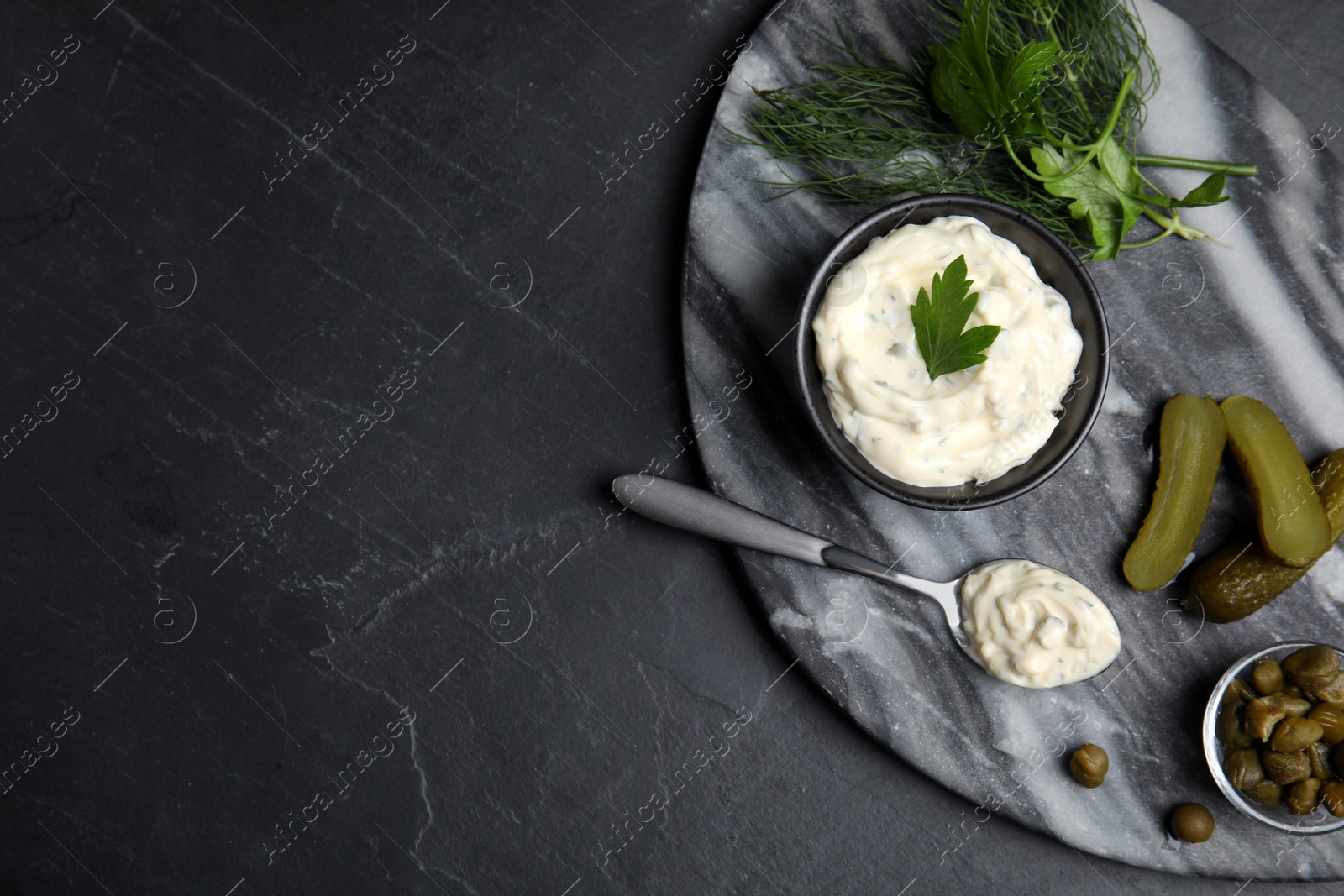 Photo of Tasty tartar sauce and ingredients on black table, top view. Space for text