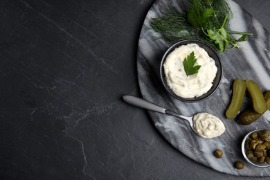 Photo of Tasty tartar sauce and ingredients on black table, top view. Space for text