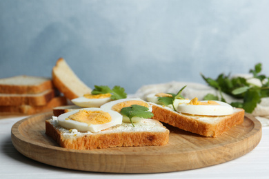 Photo of Tasty sandwiches with boiled eggs on wooden tray, closeup