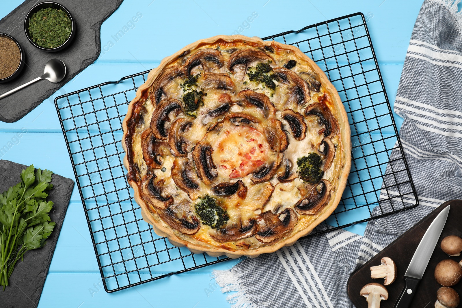 Photo of Delicious quiche with mushrooms and ingredients on light blue wooden table, flat lay