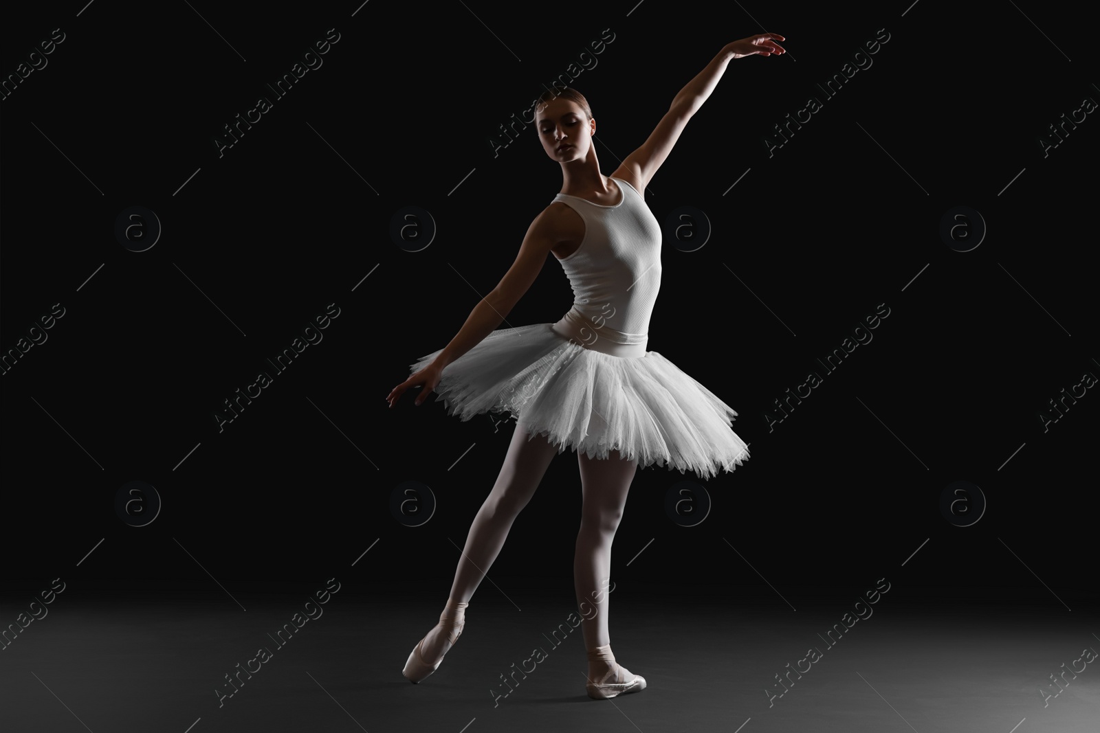 Photo of Young ballerina practicing dance moves on black background