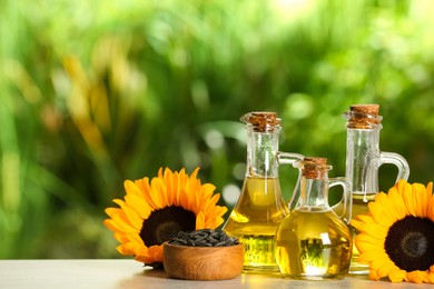 Photo of Sunflower cooking oil, seeds and yellow flowers on light grey table outdoors, space for text