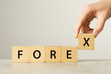 Photo of Woman making word Forex with wooden cubes on light table against white background, closeup