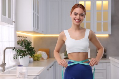 Photo of Slim woman measuring waist with tape in kitchen. Weight loss