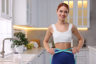 Slim woman measuring waist with tape in kitchen. Weight loss