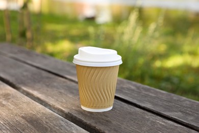 Photo of Paper cup on wooden bench outdoors. Coffee to go