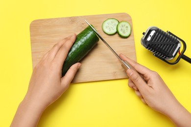 Photo of Woman making ASMR sounds with microphone and cucumber on yellow background, top view