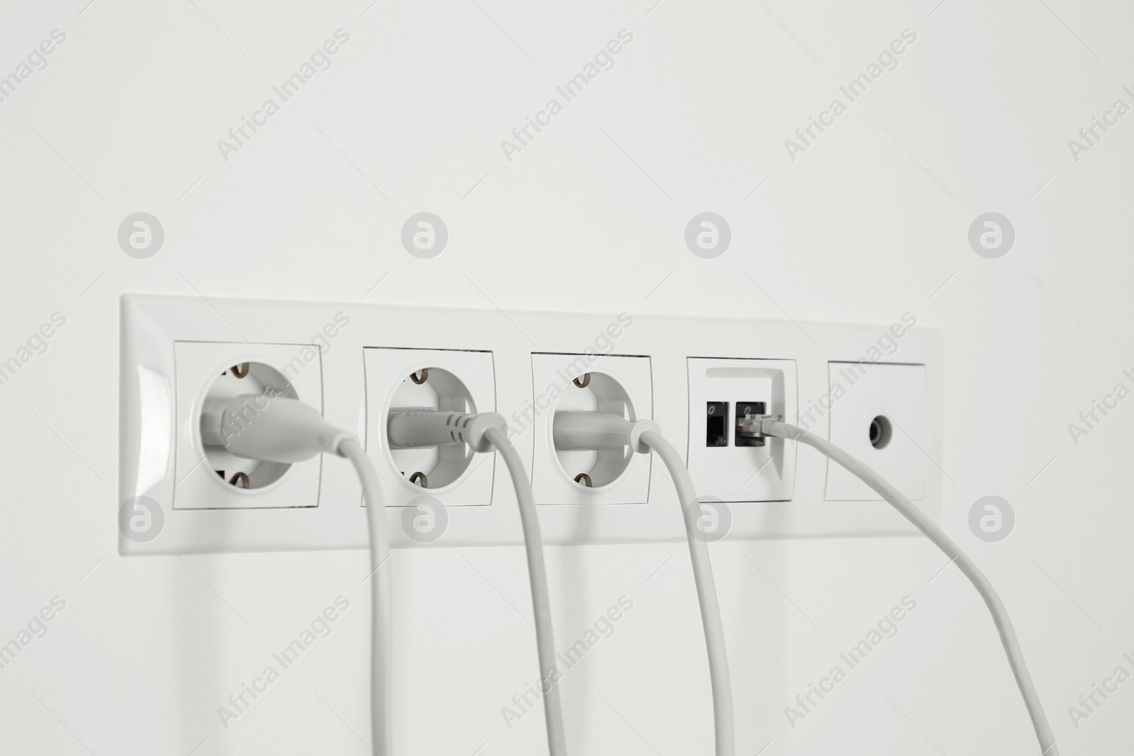 Photo of Many power sockets with plugs, ethernet and TV coax plates on white wall indoors