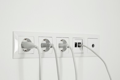 Photo of Many power sockets with plugs, ethernet and TV coax plates on white wall indoors
