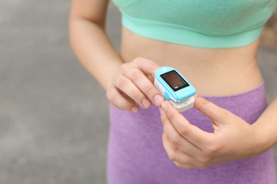 Photo of Young woman checking pulse with medical device after training on street, closeup. Space for text