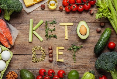 Photo of Phrase Keto Diet made with products surrounded by different food on wooden table, flat lay