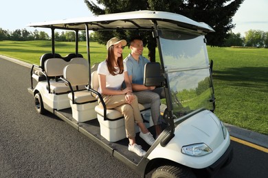 Photo of Happy couple driving golf cart on road in park
