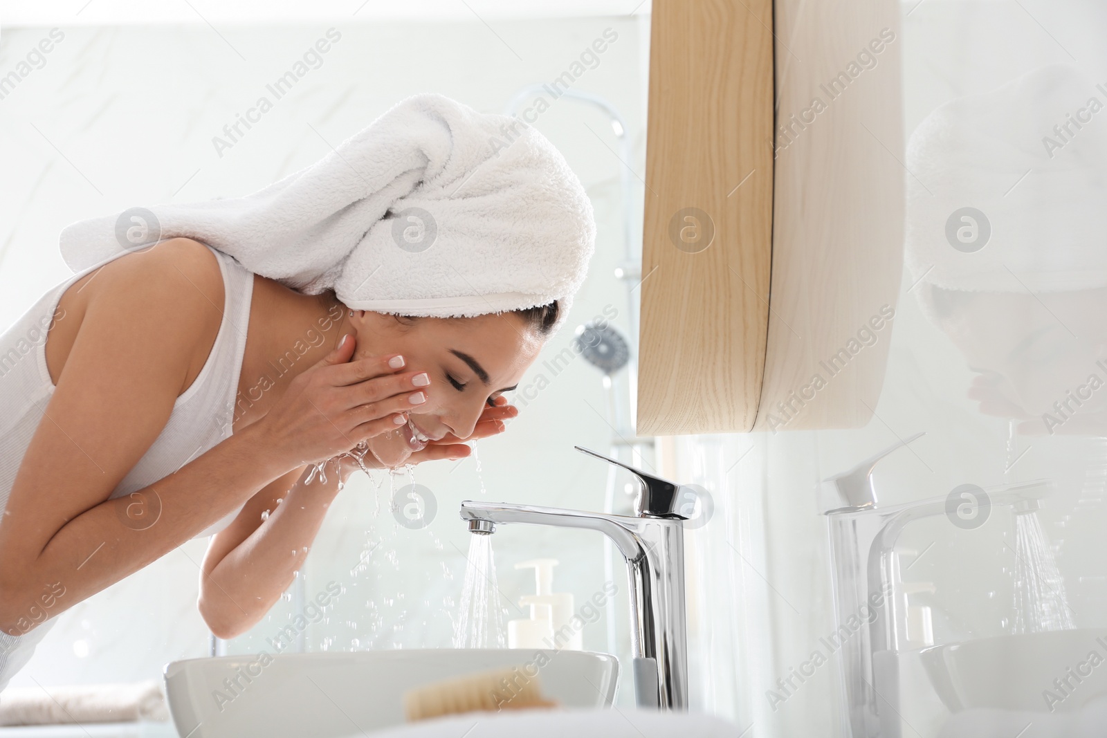 Photo of Happy young woman washing face in bathroom