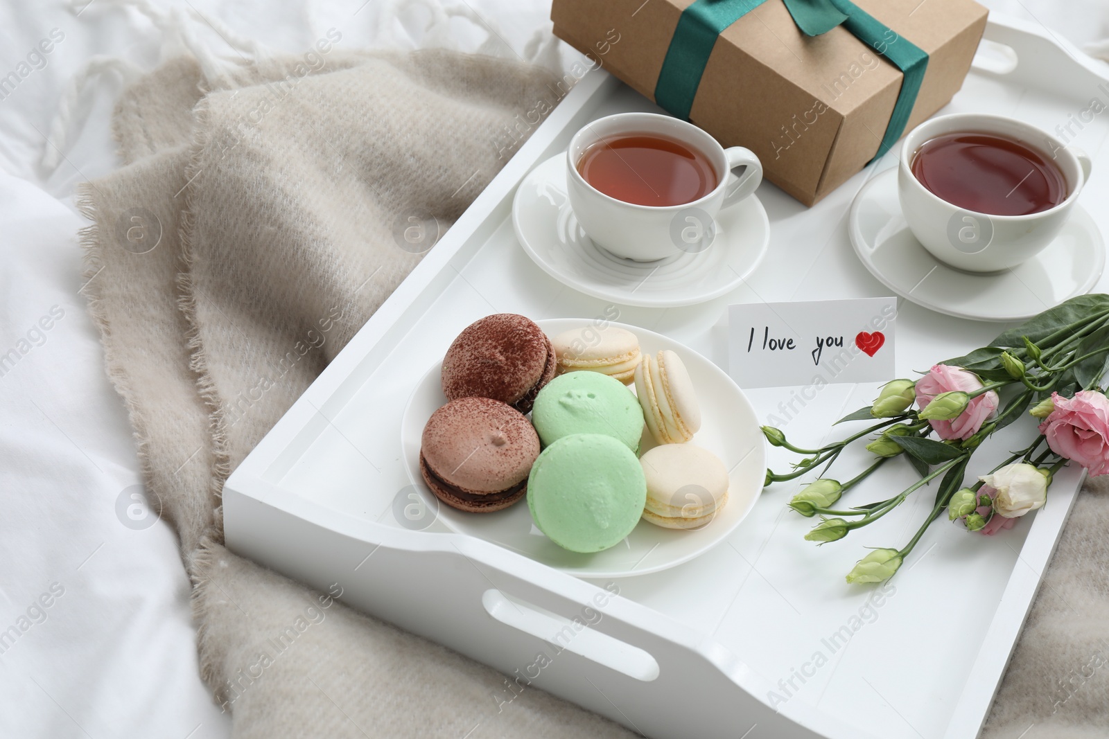 Photo of Tasty breakfast served in bed. Delicious macarons, tea, gift box, flowers and I Love You card on tray